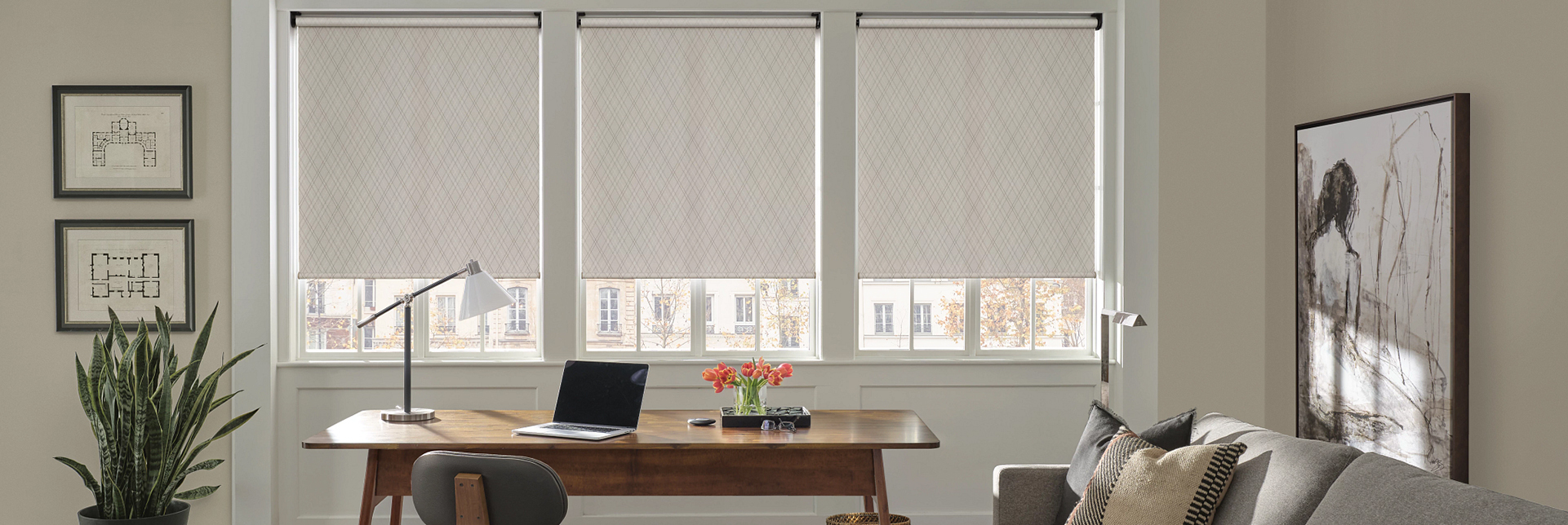 A stylish home office with a modern desk, chair, and three large windows adorned with elegant designer roller shades, providing privacy and diffused light.